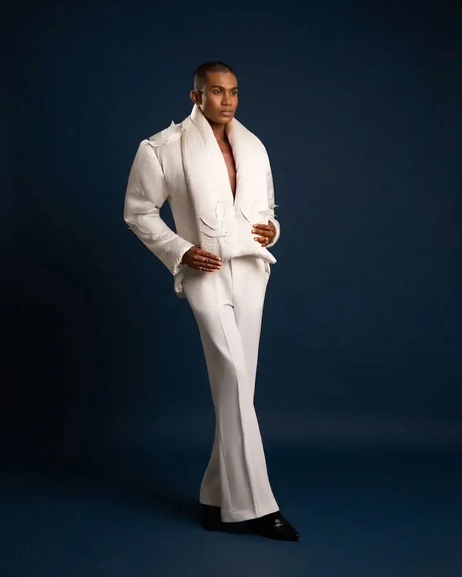 Model in a white draped avant-garde suit against a navy studio backdrop