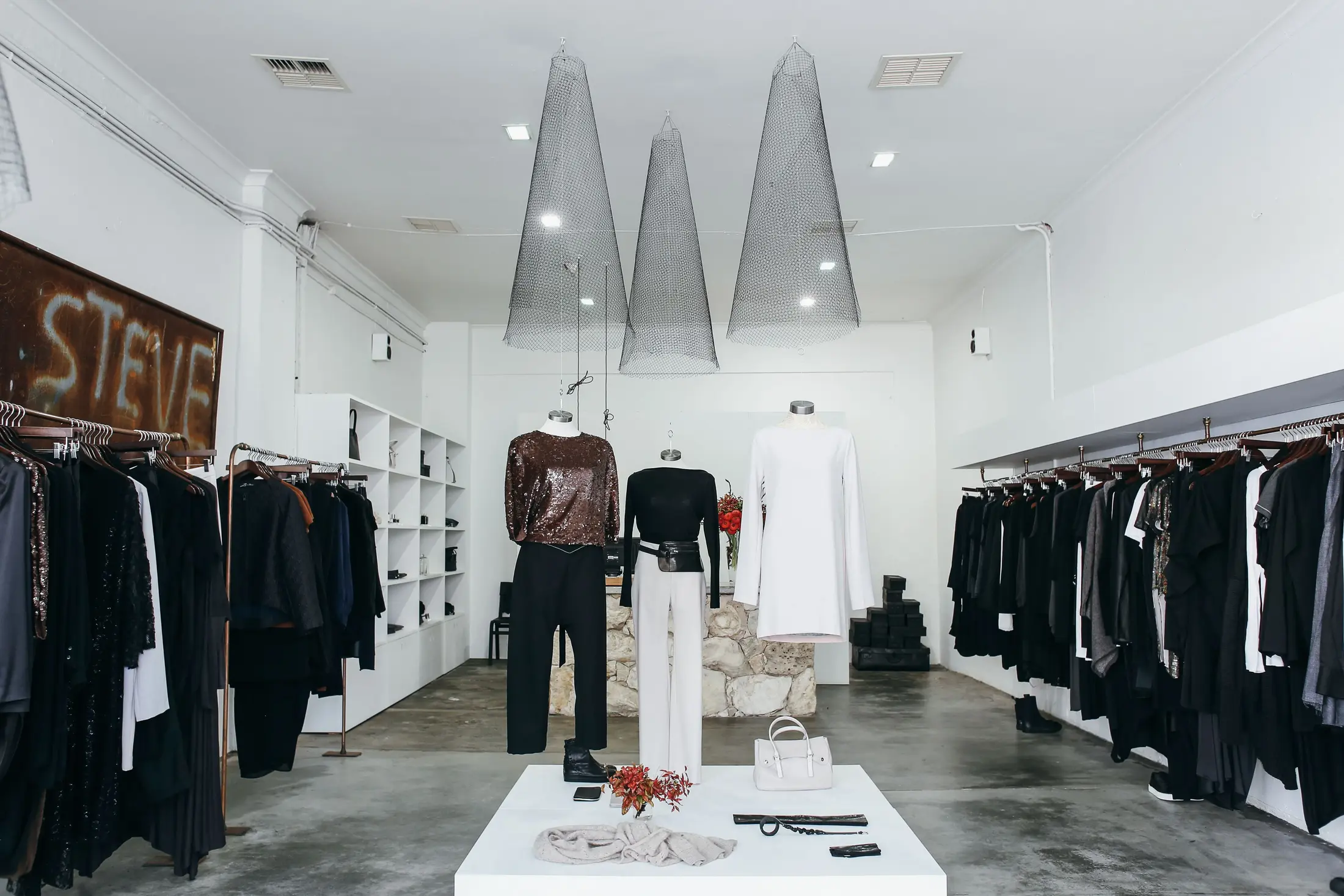 A boutique retail interior with pendant lights over clothing racks and mannequins