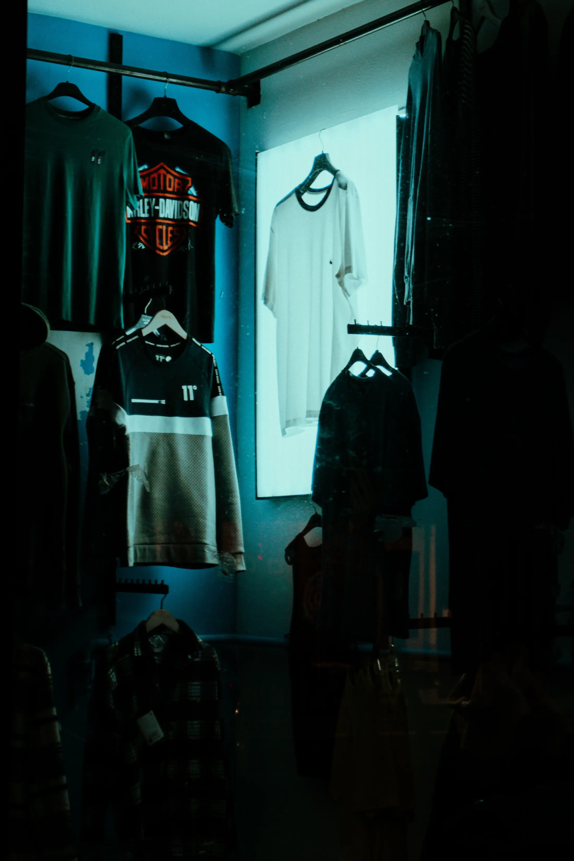 A walk-in closet with shirts hanging under teal ambient lighting